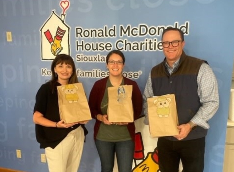 3 volunteers standing with brown bags in front of Ronald McDonald House Charities backdrop