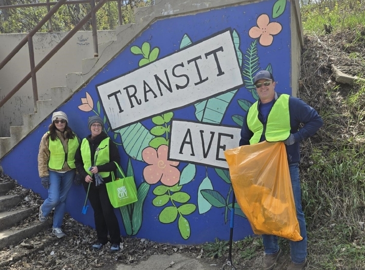 Three volunteers posing by sign with trash pick up supplies